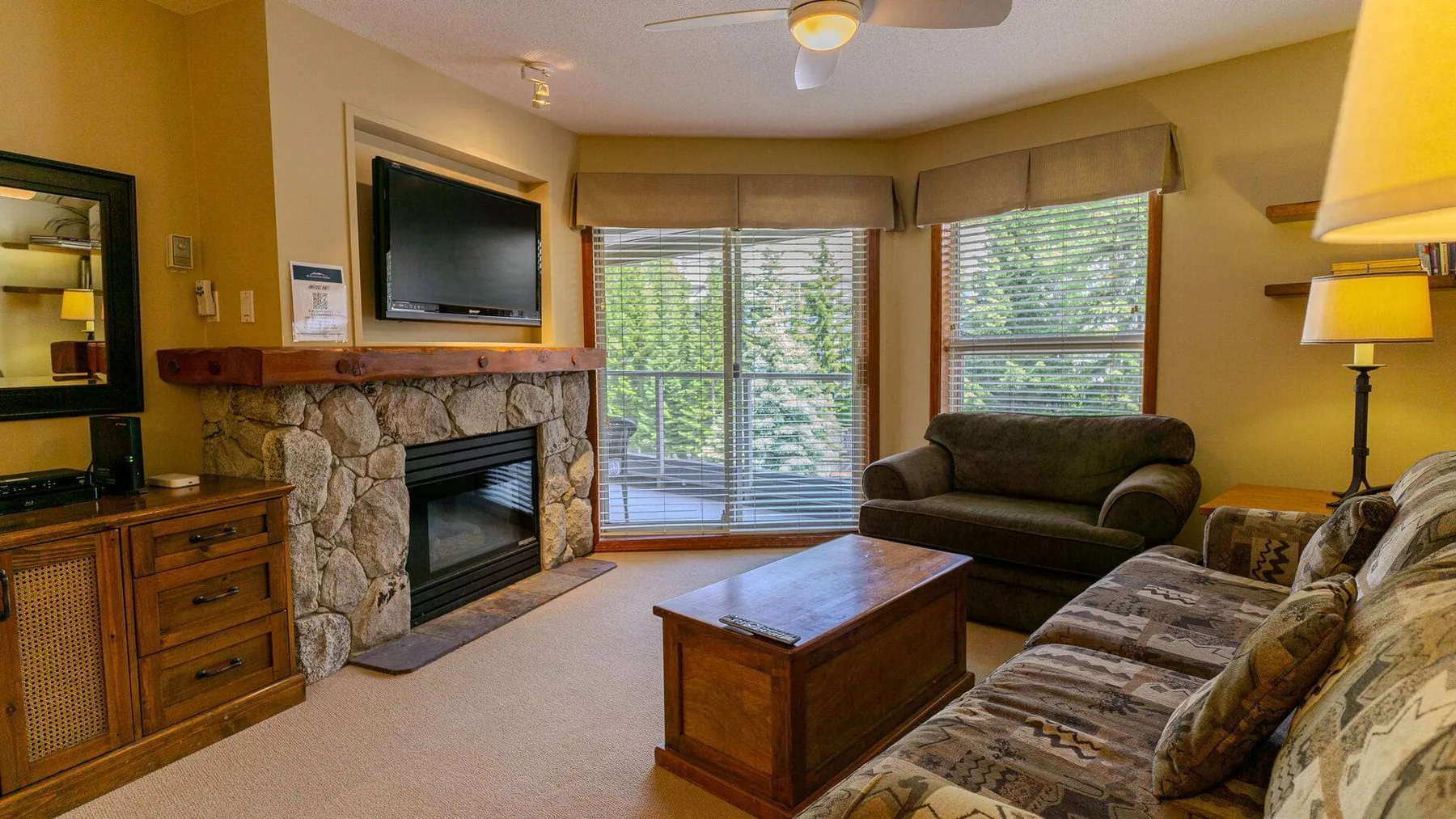 A living room with a stone fireplace, seating, and large windows.