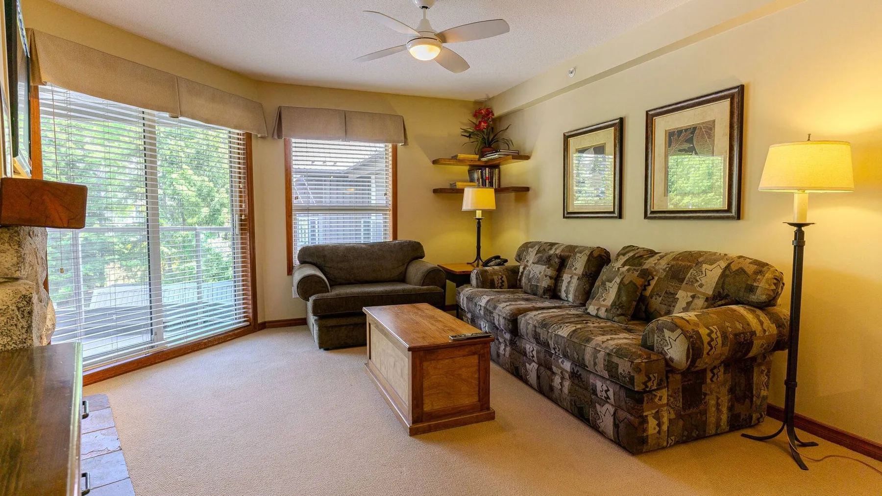 A living room with patterned seating, a wooden coffee table, and large windows.