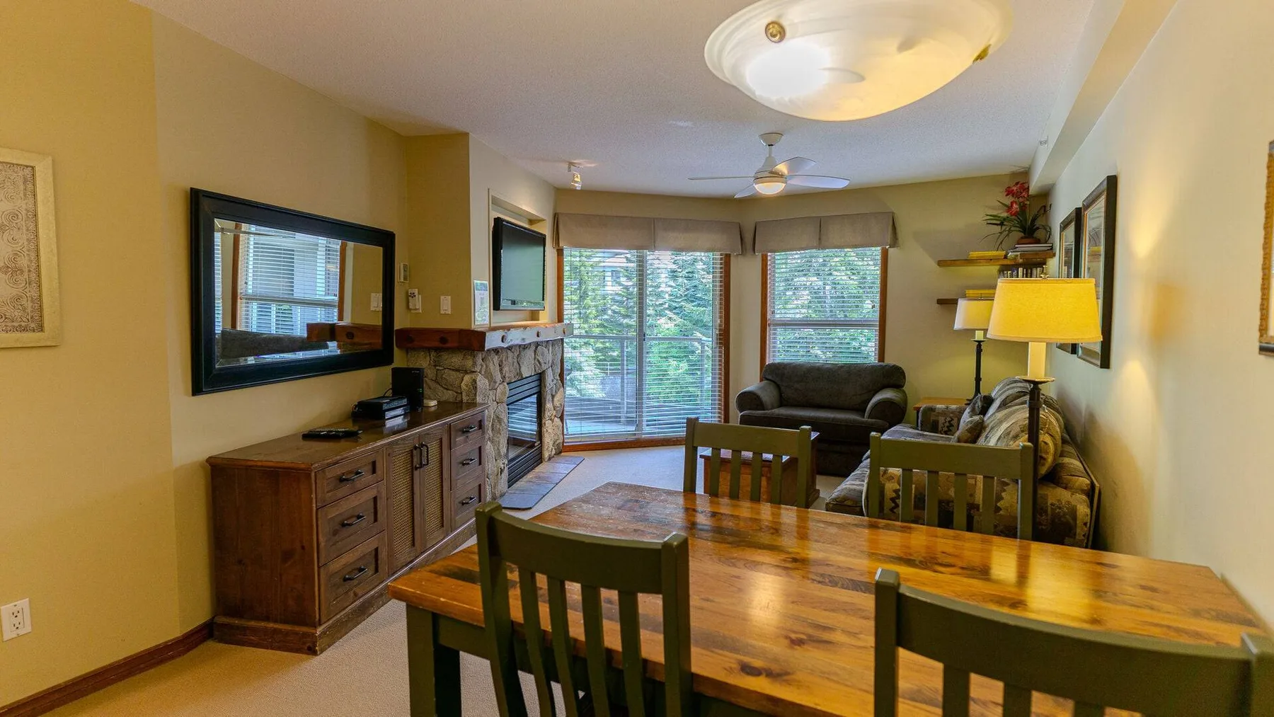 A dining and living area with a wooden table, seating, and windows.