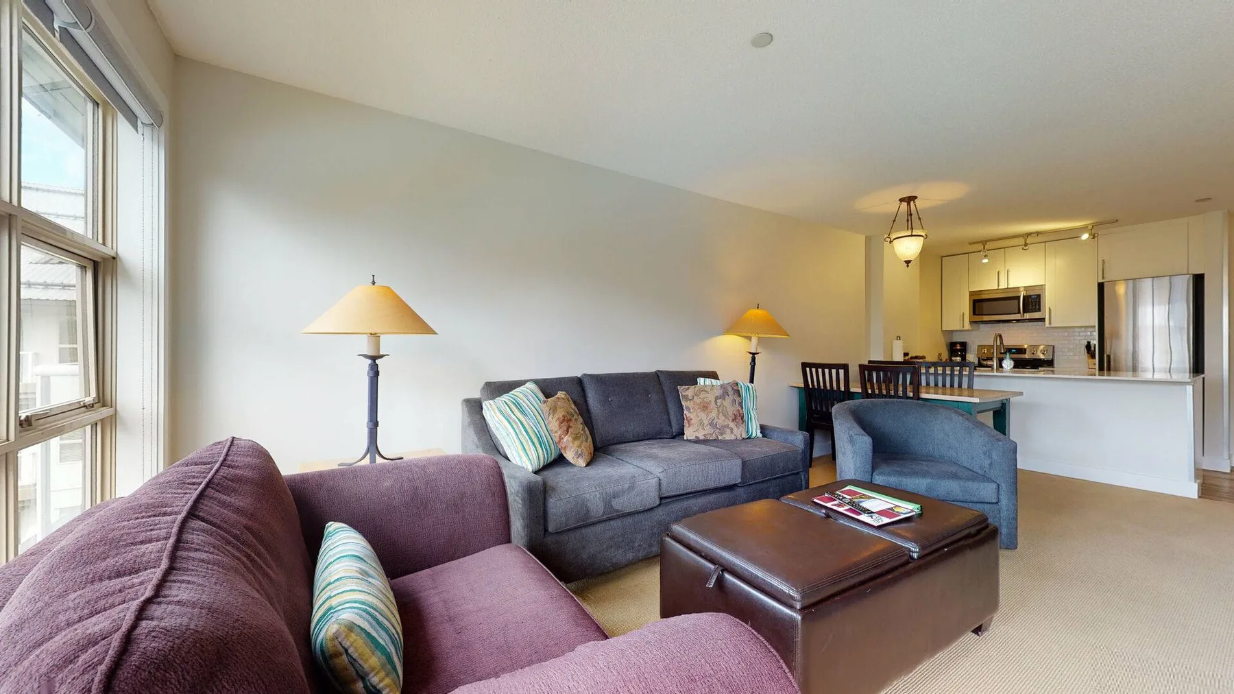 A living room with a sofa, armchairs, and a coffee table beside large windows.