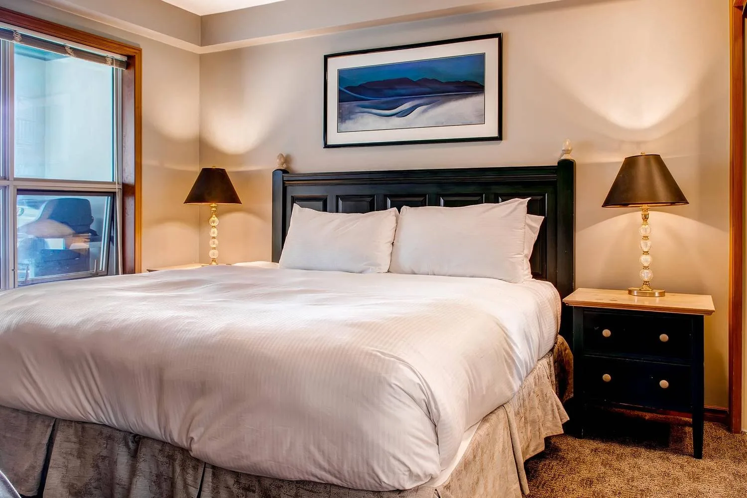 A bedroom with a large bed, bedside tables, and a framed picture above the headboard.