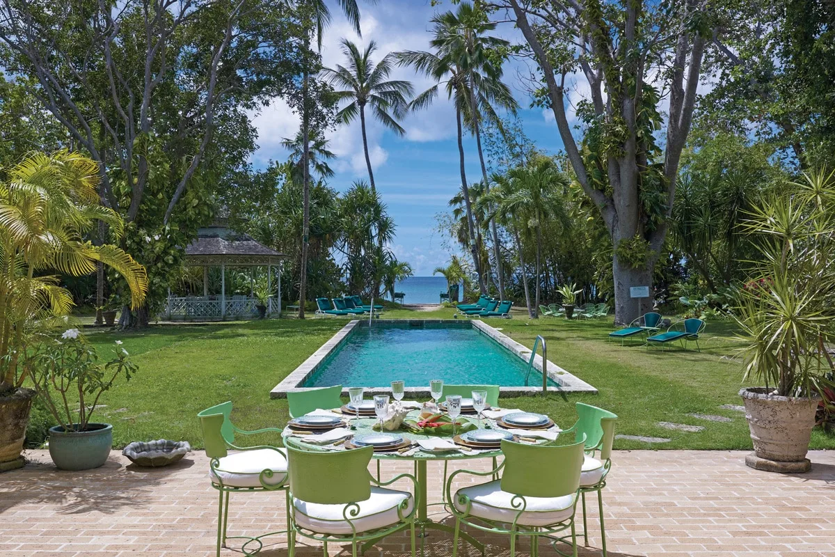 Una piscina y una mesa de comedor al aire libre están entre palmeras junto al mar.