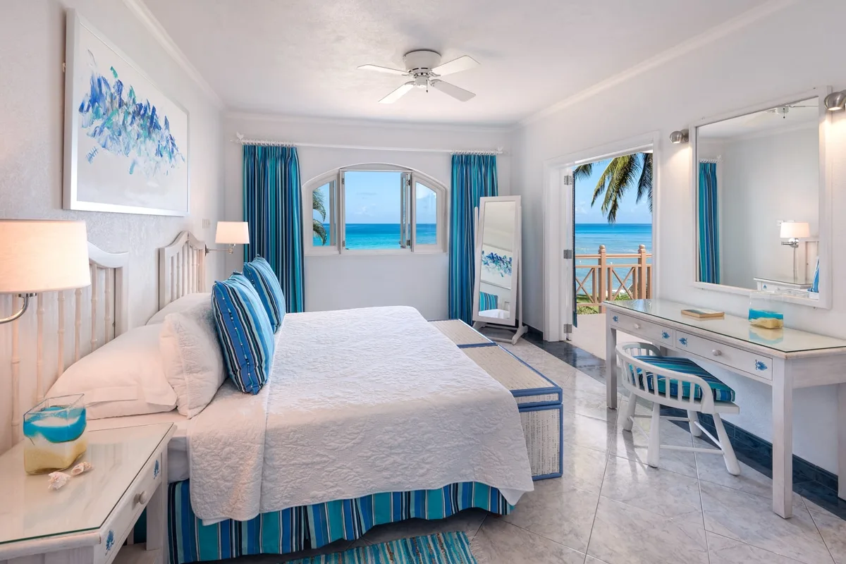 A bright bedroom with a bed, blue curtains, and ocean views through the windows.