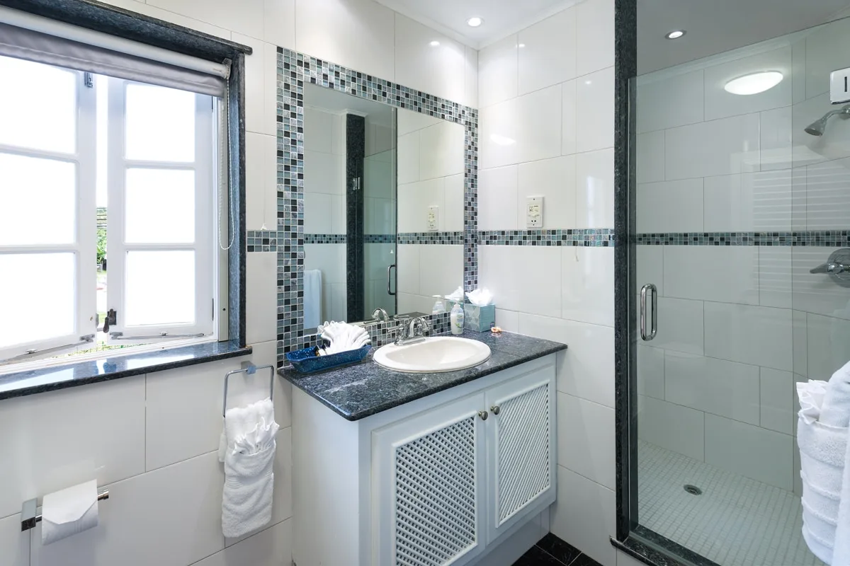 A bright bathroom with a sink vanity, mirror, and glass shower.