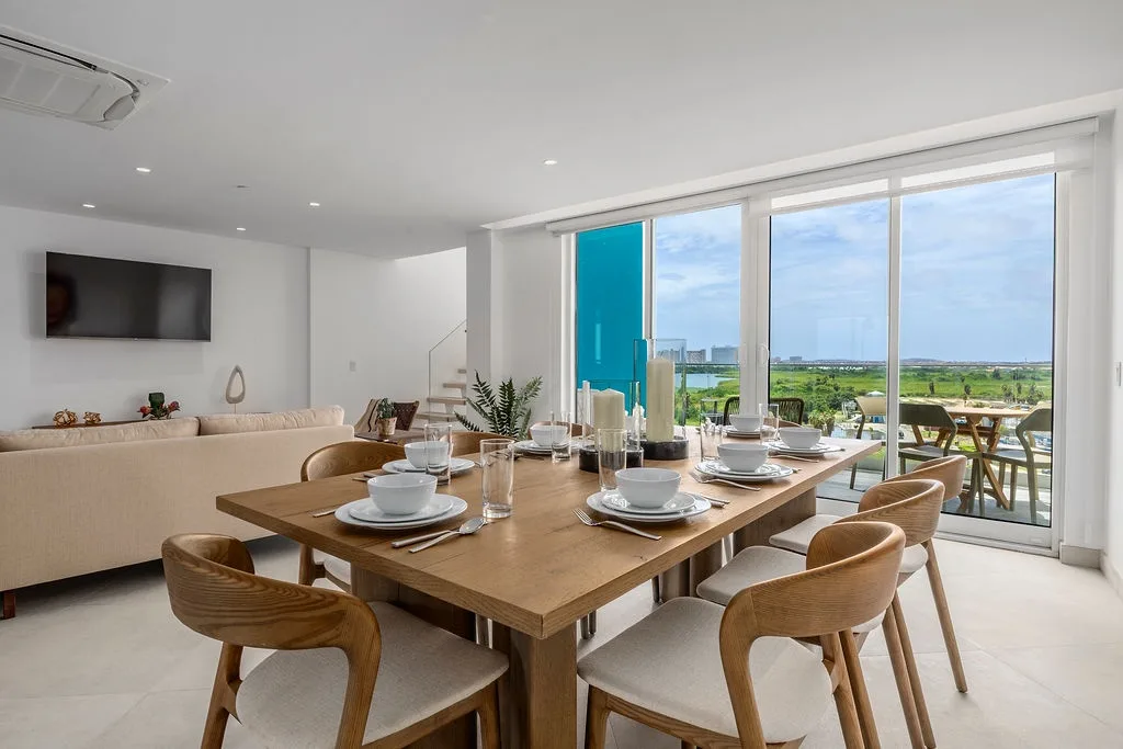 Mesa de comedor puesta para seis, con luz natural y vistas a zonas verdes.
