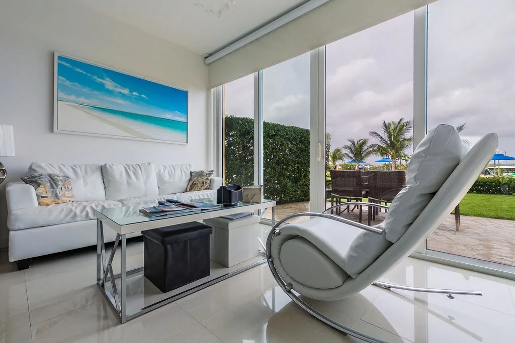 Acomódate en el mullido sofá blanco o en la elegante mecedora mientras la luz natural inunda tu espacio a través de ventanas de piso a techo que enmarcan vistas de la exuberante vegetación tropical y de la piscina cercana.