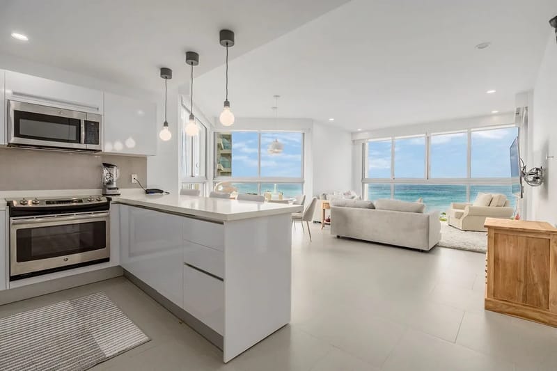 Su refugio frente al océano cuenta con una elegante cocina blanca integrada en una luminosa sala de estar con impresionantes vistas al mar a través de ventanas de piso a techo.