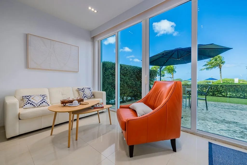 Living room with floor-to-ceiling windows overlooking gardens and palms.
