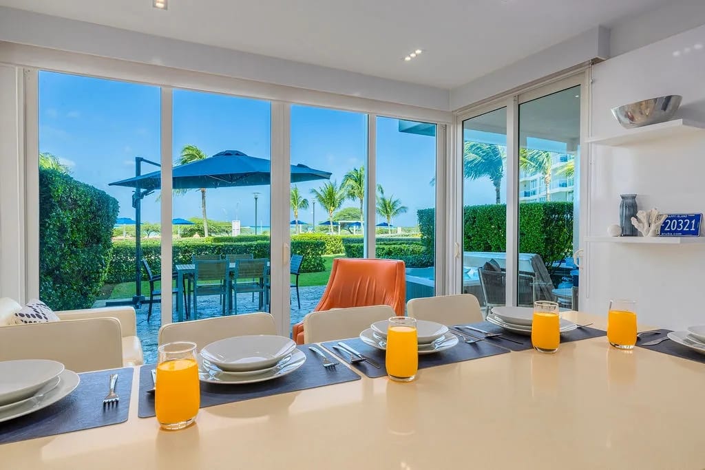 Dining table with pool and tropical views through floor-to-ceiling windows.