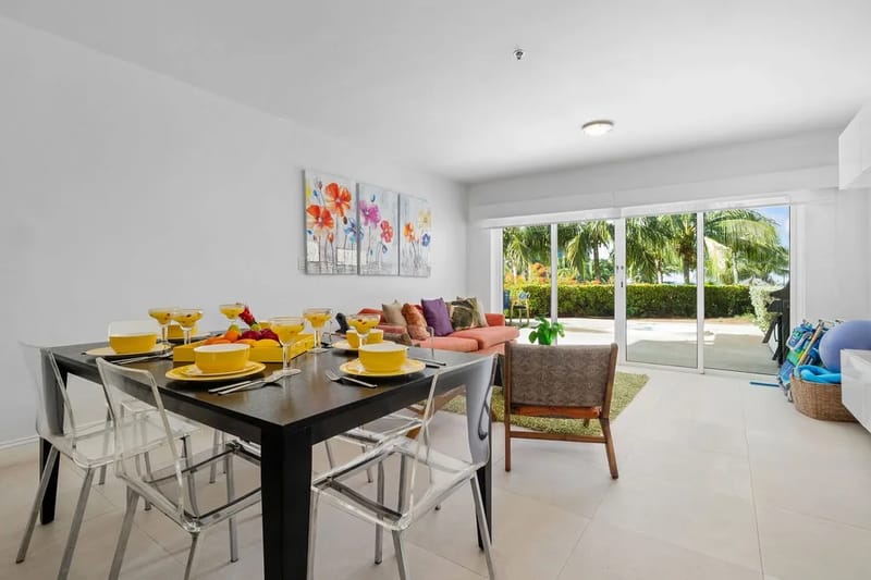 Espacio abierto de sala de estar y comedor con puertas de vidrio y vistas tropicales.