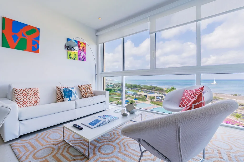 Tu luminosa sala de estar, decorada con arte, enmarca impresionantes vistas al mar y a la costa a través de ventanales de piso a techo: perfecta para relajarte en cómodos asientos mientras disfrutas del sereno paisaje frente a la playa.