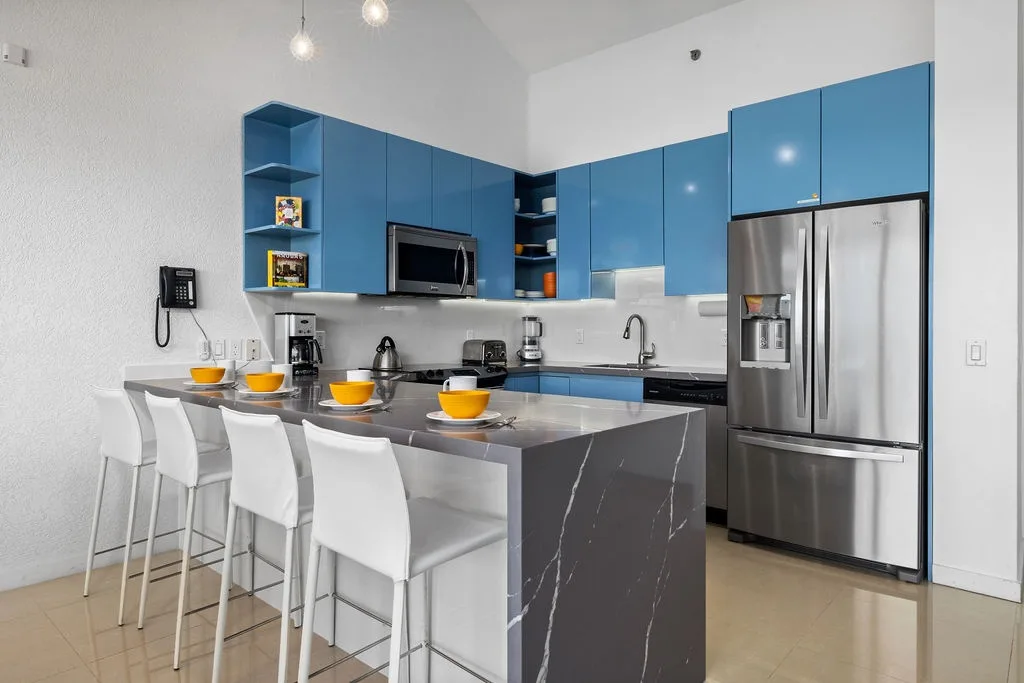 Tu moderna cocina te espera con elegantes electrodomésticos de acero inoxidable, llamativos gabinetes azules y una acogedora barra de desayuno donde puedes reunirte para tomar el café de la mañana y planear las aventuras del día.