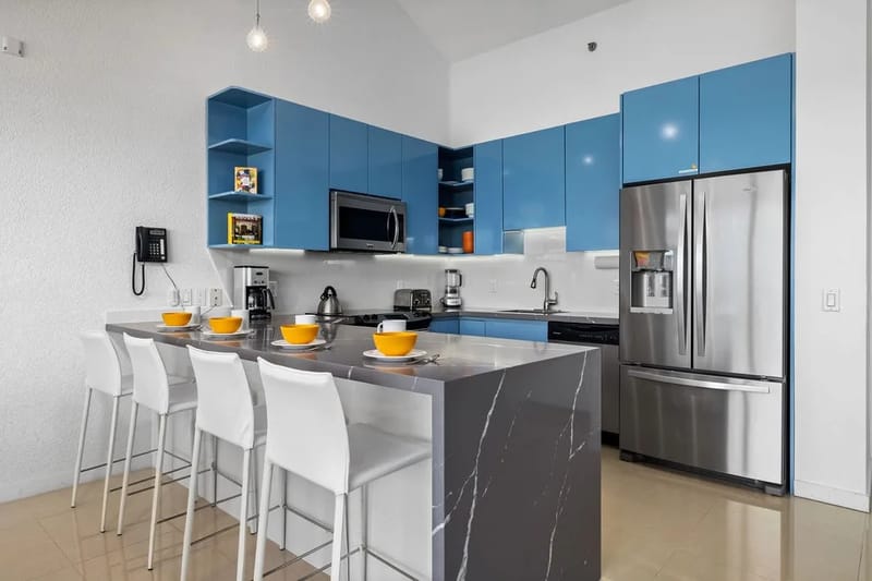 Tu moderna cocina te espera con elegantes electrodomésticos de acero inoxidable, llamativos gabinetes azules y una acogedora barra de desayuno donde puedes reunirte para tomar el café de la mañana y planear las aventuras del día.