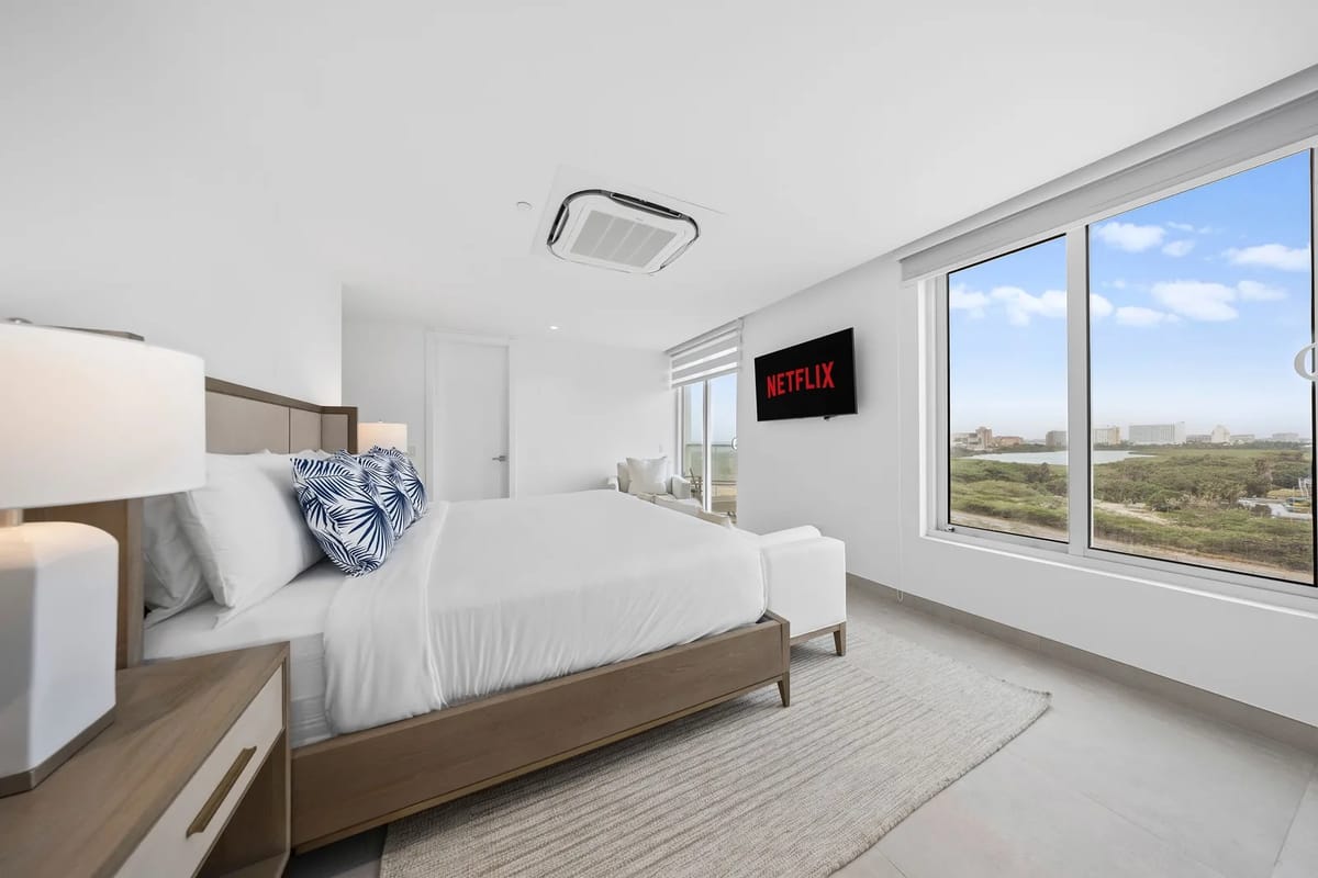 Tu dormitorio luminoso y moderno cuenta con ropa de cama impecable, un televisor montado y grandes ventanales que enmarcan vistas despejadas del paisaje, perfecto para descansar después de explorar.