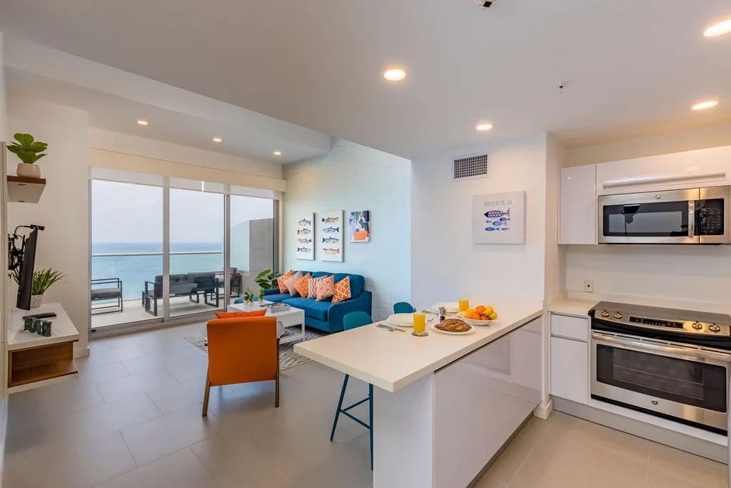 Tu espacio luminoso y moderno conecta de forma fluida la cocina con la sala de estar, con impresionantes vistas al mar a través de ventanas de piso a techo y un balcón privado a solo unos pasos.