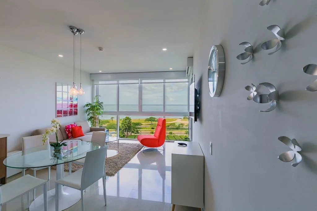 Sala de estar y comedor con vistas frente a la playa, muebles de líneas elegantes y colores vibrantes.