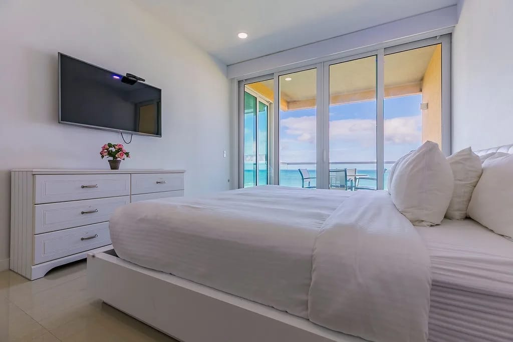 Bedroom with white linens and a private balcony overlooking turquoise waters.