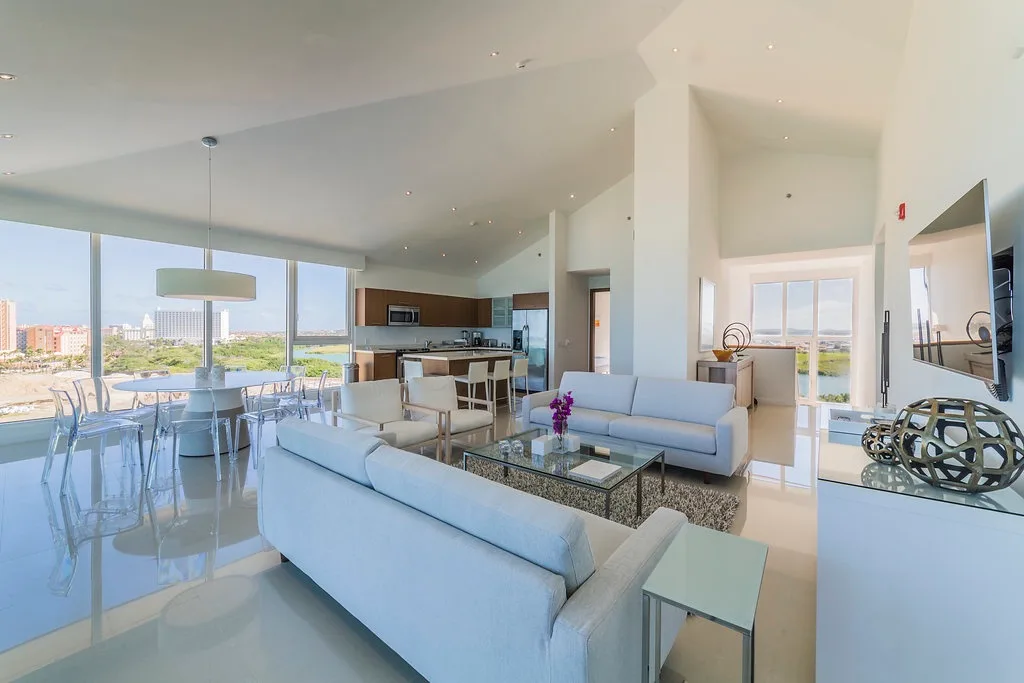 Step into this bright, open-concept living space with floor-to-ceiling windows, sofas, a dining table, and a modern kitchen.