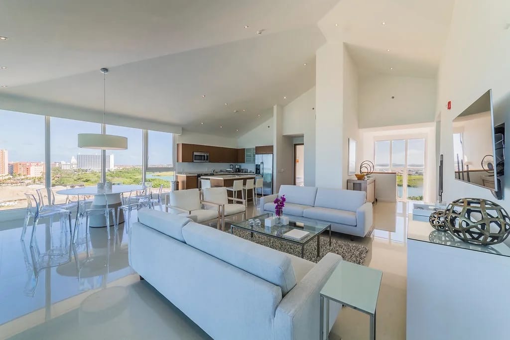 Step into this bright, open-concept living space with floor-to-ceiling windows, sofas, a dining table, and a modern kitchen.