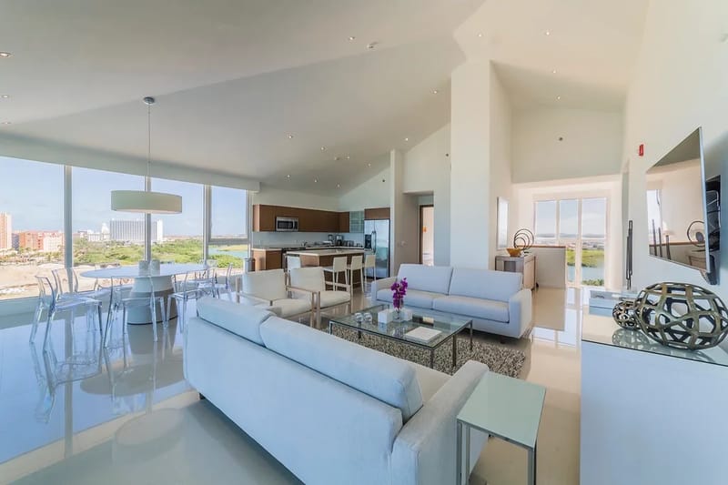 Step into this bright, open-concept living space with floor-to-ceiling windows, sofas, a dining table, and a modern kitchen.