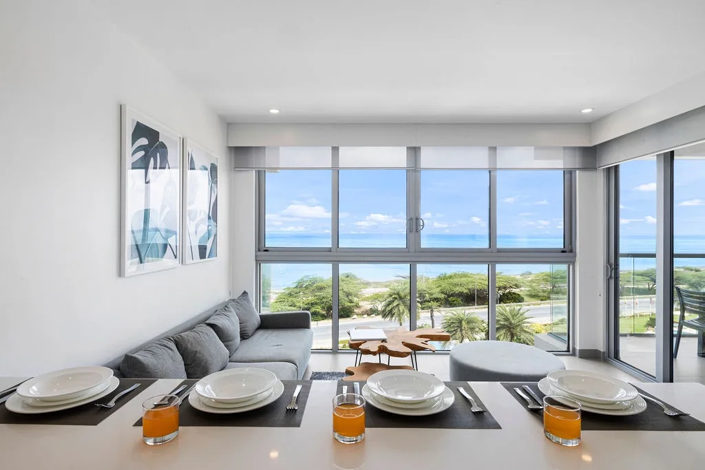 Sala de estar y comedor luminosos y modernos con amplias vistas al mar. Relájese en cómodos asientos mientras disfruta de la brisa costera y la vegetación tropical justo al otro lado de las ventanas.