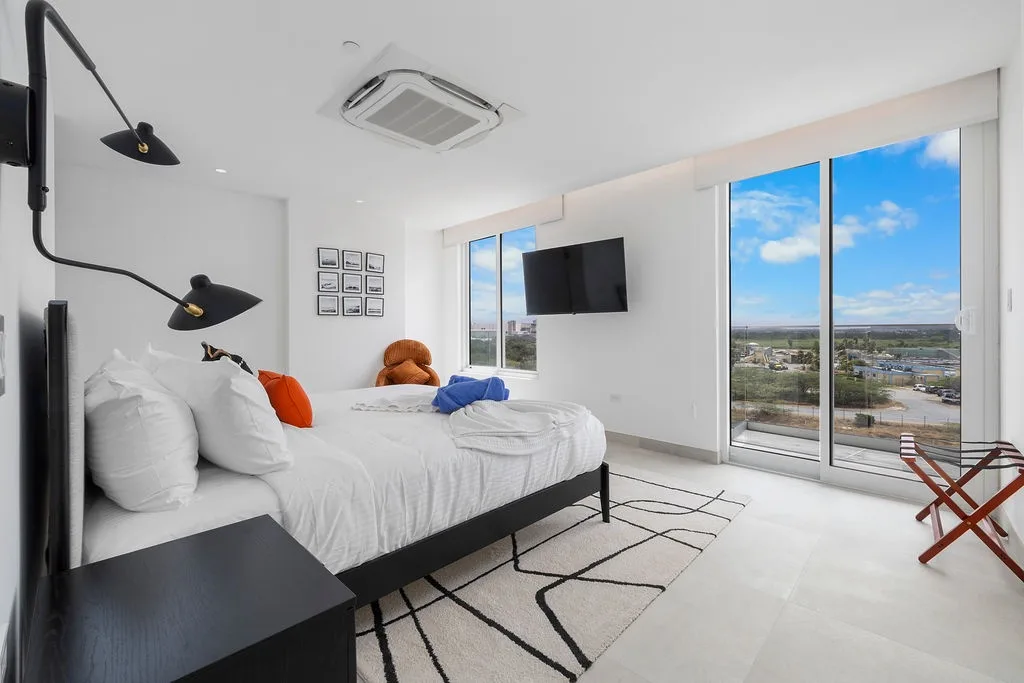 Step into your sunlit retreat where crisp white linens beckon and floor-to-ceiling windows frame endless sky views. Modern comforts like a wall-mounted TV and climate control ensure your stay is relaxing.