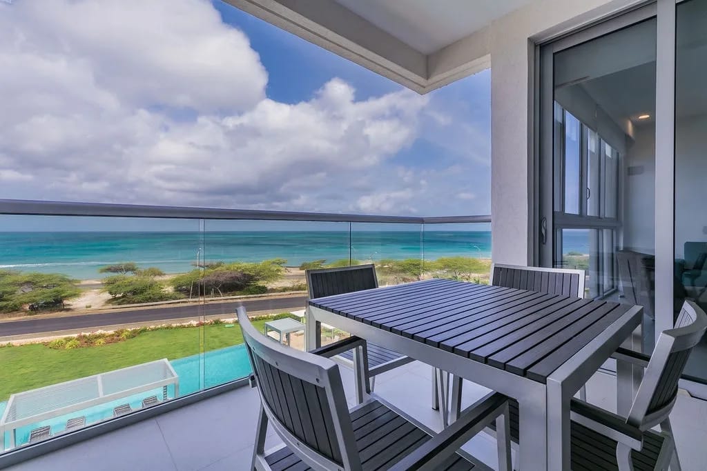 Modern balcony overlooking turquoise ocean waters and coastal greenery.