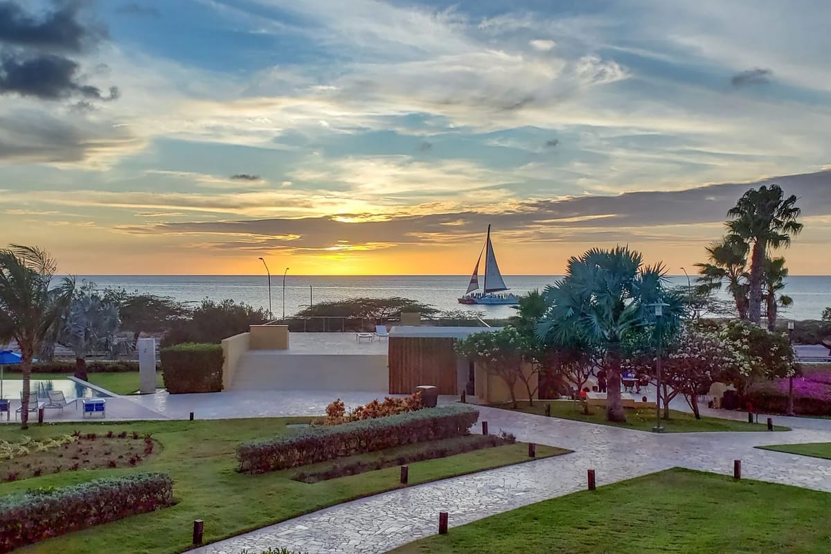 La propiedad cuenta con jardines tropicales bien cuidados y senderos que conducen hacia la orilla del mar, con un velero que pasa al atardecer: un entorno costero sereno para relajarse.