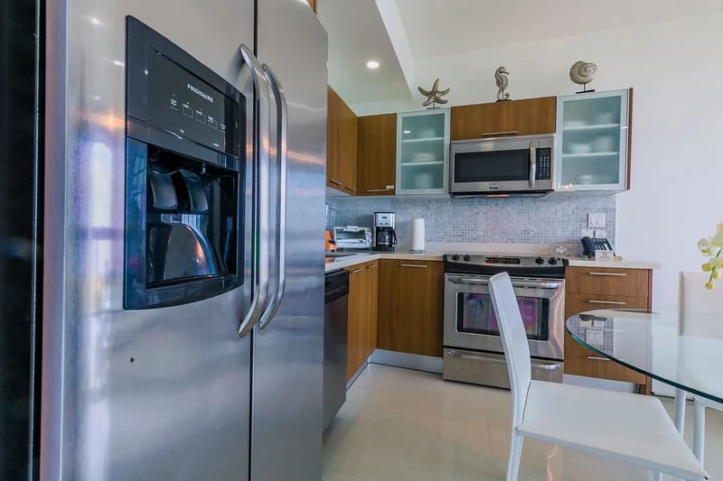Cocina con electrodomésticos de acero inoxidable, gabinetes de madera y una mesa de comedor con cubierta de vidrio.