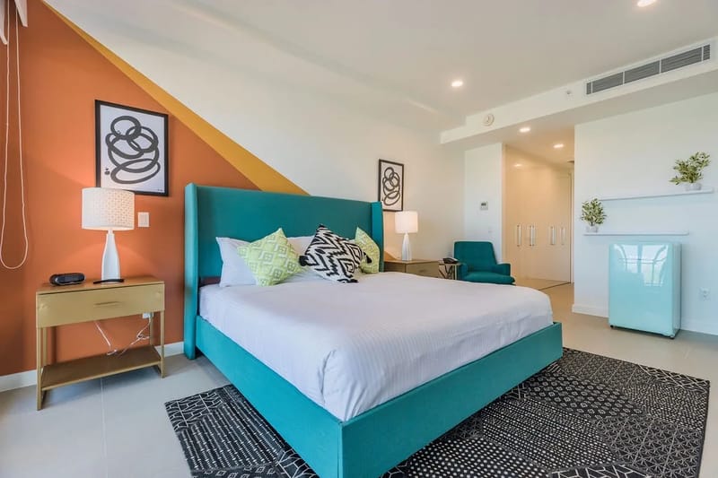 Sumérgete en la mullida cama de color verde azulado, rodeada de obras de arte llamativas y detalles modernos: tu refugio de descanso te espera con sábanas impecables y un estilo vibrante.