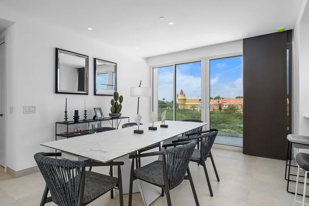 This bright dining area features a sleek marble table and stylish chairs, with large windows framing views of the surrounding neighborhood and historic buildings beyond.