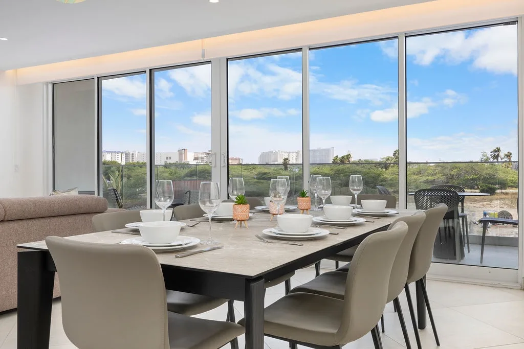 Reúnanse alrededor de esta elegante mesa de comedor preparada para seis personas, con amplias vistas de la exuberante vegetación y del paisaje urbano a lo lejos a través de ventanales de piso a techo.