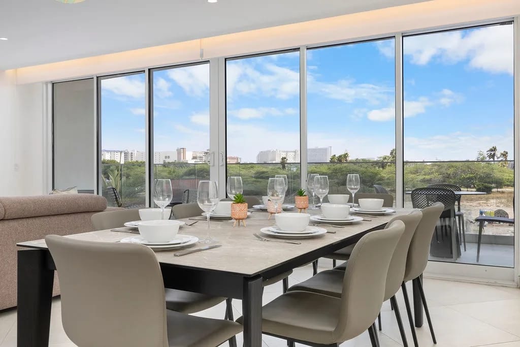 Reúnanse alrededor de esta elegante mesa de comedor preparada para seis personas, con amplias vistas de la exuberante vegetación y del paisaje urbano a lo lejos a través de ventanales de piso a techo.