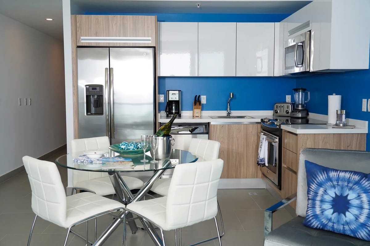 Cocina moderna con detalles azules y mesa de comedor de vidrio.