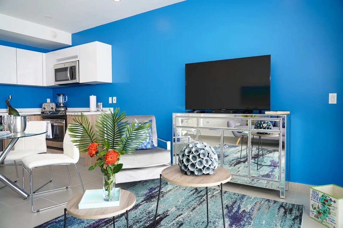Sala de estar de planta abierta con paredes azules, cocina, sofá y entretenimiento.