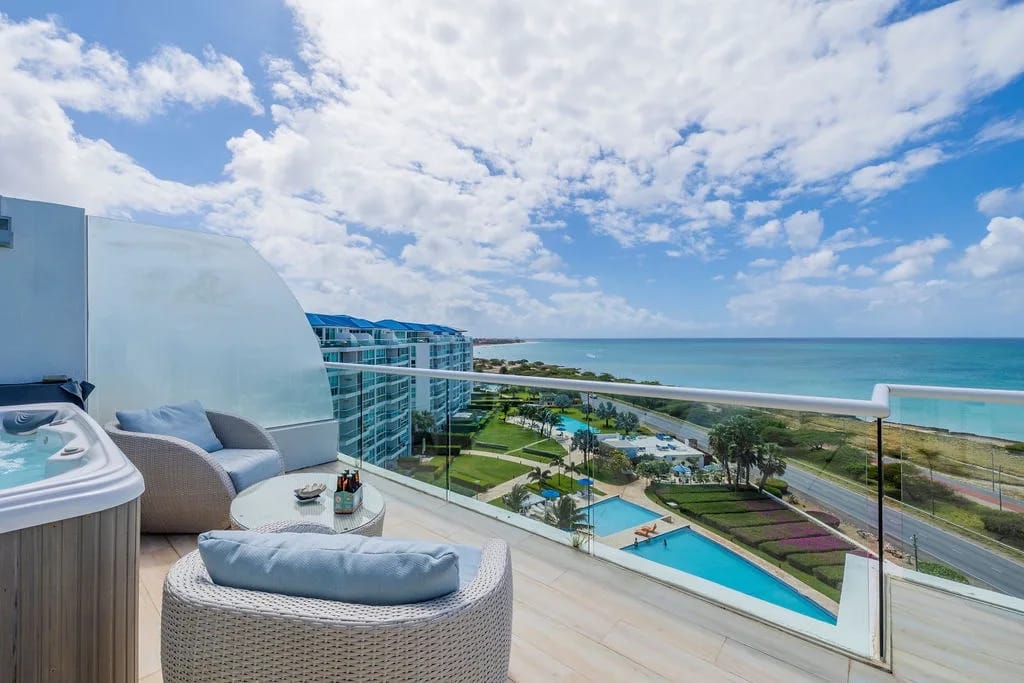 El balcón de este penthouse ofrece un impresionante entorno frente a la playa, donde las aguas turquesas se encuentran con arenas prístinas. Su jacuzzi privado le espera a cielo abierto, mientras que los cómodos asientos de descanso le invitan a relajarse con amplias vistas de la costa.