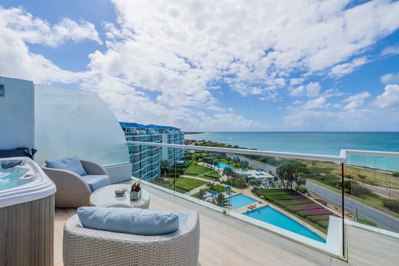 This penthouse balcony offers a stunning beachfront setting where turquoise waters meet pristine sands. Your private hot tub awaits under open skies, while plush lounge seating invites you to unwind with sweeping coastal views.