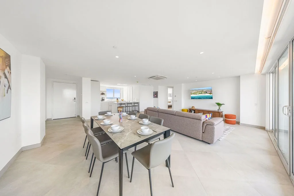 Bright, open-plan living space with a dining table, sofa, and floor-to-ceiling windows.