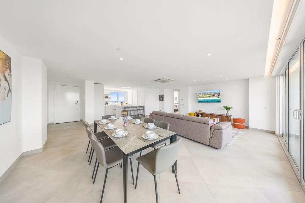 Bright, open-plan living space with a dining table, sofa, and floor-to-ceiling windows.
