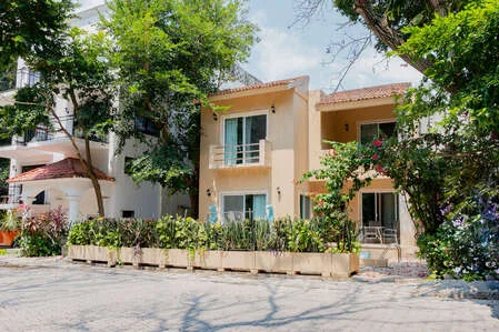 Una casa de dos plantas se encuentra detrás de un seto bajo y árboles frondosos.