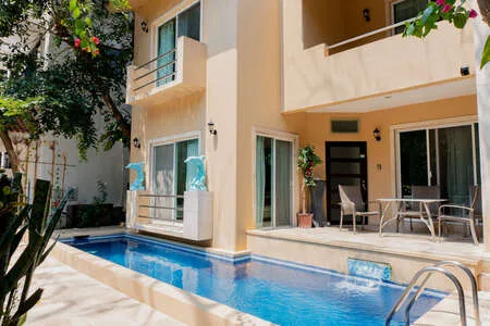 Una piscina soleada en un patio junto a un edificio claro con asientos al aire libre.