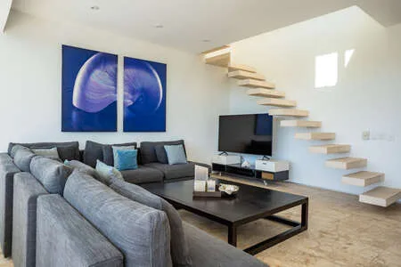 Una sala luminosa con asientos grises, un televisor y una escalera.