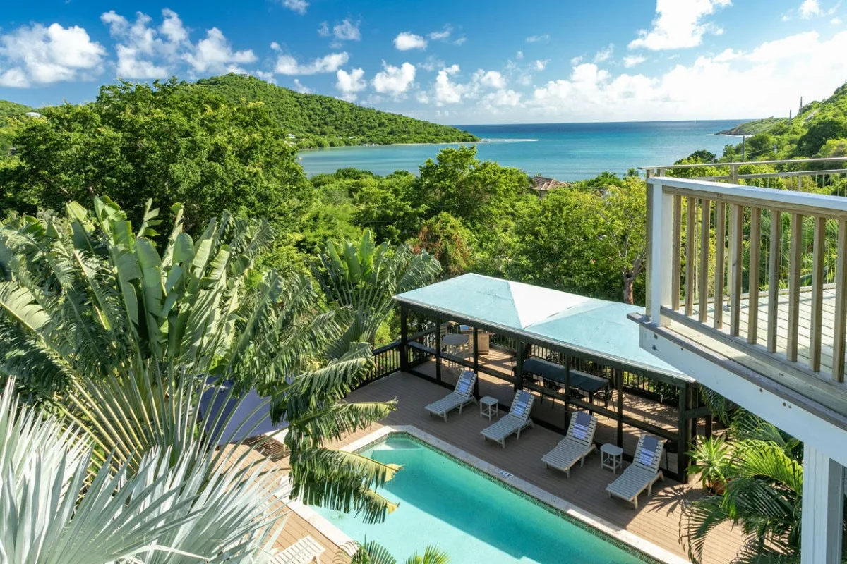 Una terraza junto a la piscina mira hacia vegetación frondosa y una bahía azul.