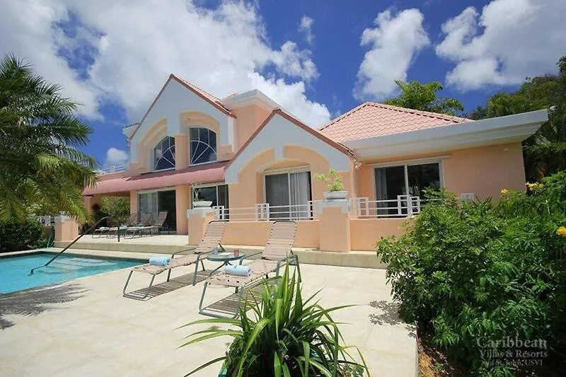A pastel-colored villa stands beside a swimming pool and patio.
