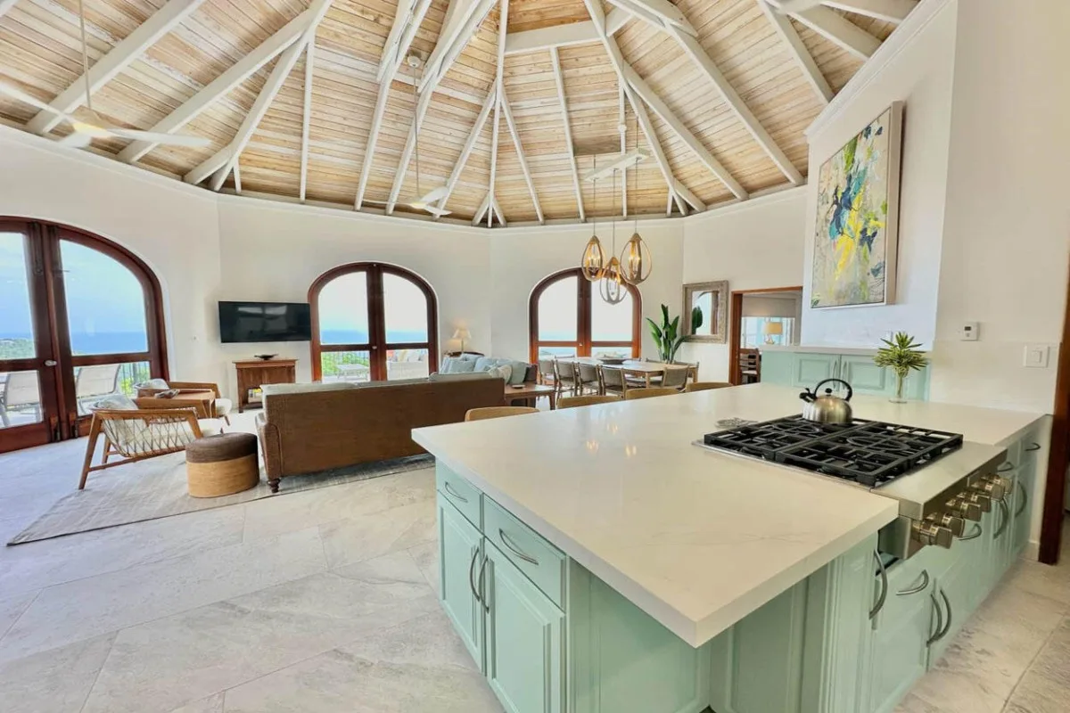 An open living, dining, and kitchen area has a large island beneath a vaulted ceiling.