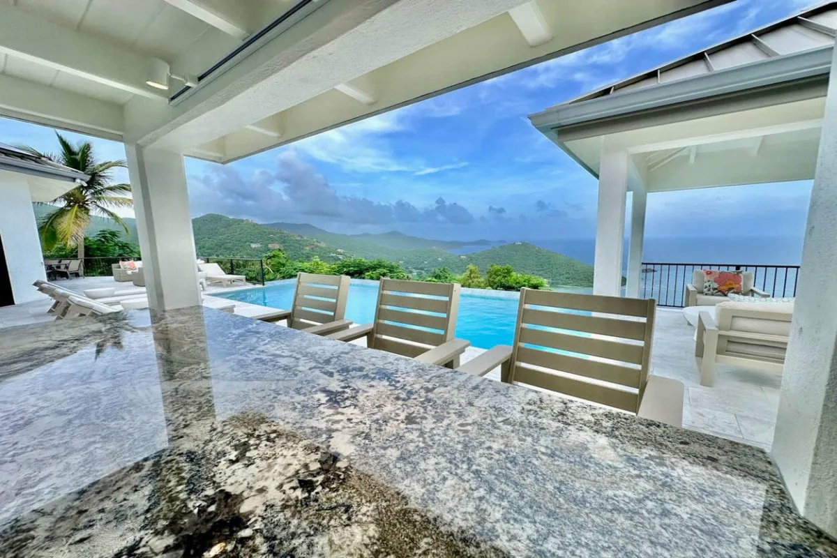 Covered outdoor counter seating overlooks a pool and a distant coastal view.