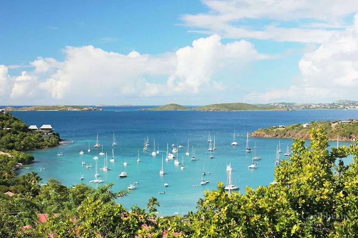 A coastal bay with boats anchored in turquoise water beneath a partly cloudy sky.