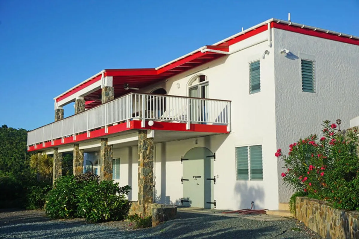 A white two-story house with red roof trim and a balcony.