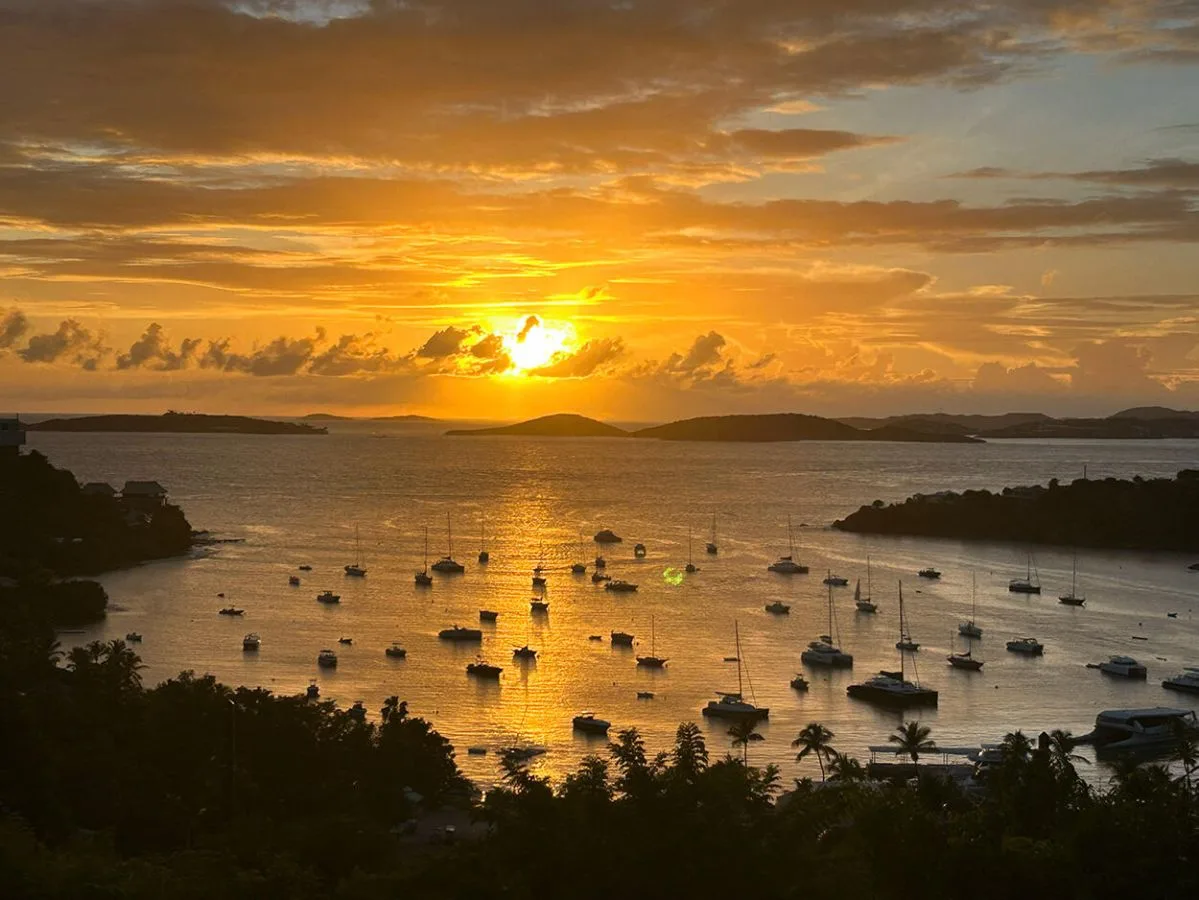 A sunset glows over a bay dotted with boats.