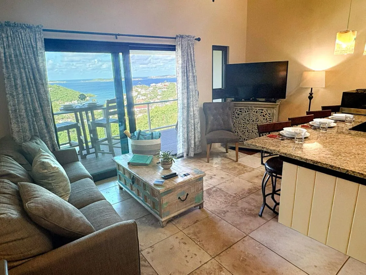 Sala de estar con asientos, televisor y vista al agua a través de puertas de vidrio.